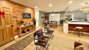 A modern living room with a wooden wall, a welcome sign, a dining area, and a kitchen with a bar. - The Ultimate Mountain Retreat - Yosemite, Bass Lake (Oakhurst)