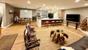 A modern living room with a sofa, a coffee table, and a TV. There is a kitchen area with a dining table and bar stools. - The Ultimate Mountain Retreat - Yosemite, Bass Lake (Oakhurst)