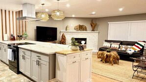 A modern kitchen with a central island, a dining area with a wooden table, and a living room with a sofa and a fireplace. - The Ultimate Mountain Retreat - Yosemite, Bass Lake (Oakhurst)