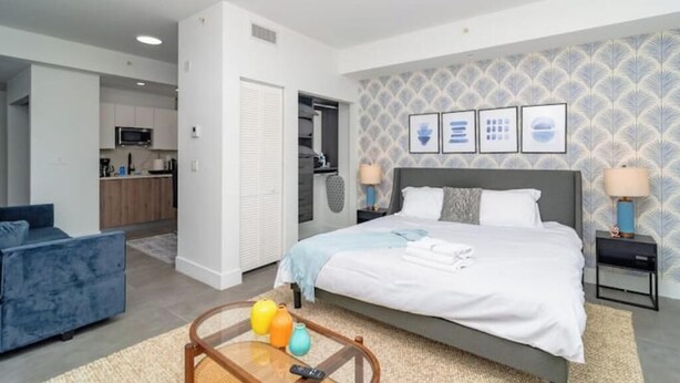Een moderne slaapkamer met een bed, nachtkastjes en een bank. Achtergrond is een keuken zichtbaar.