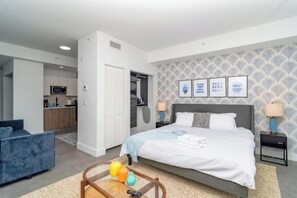 A modern bedroom with a bed, bedside tables, and a sofa. A kitchen is visible in the background. - King Bed brand new safe Oasis minutes to Brickell (Miami)