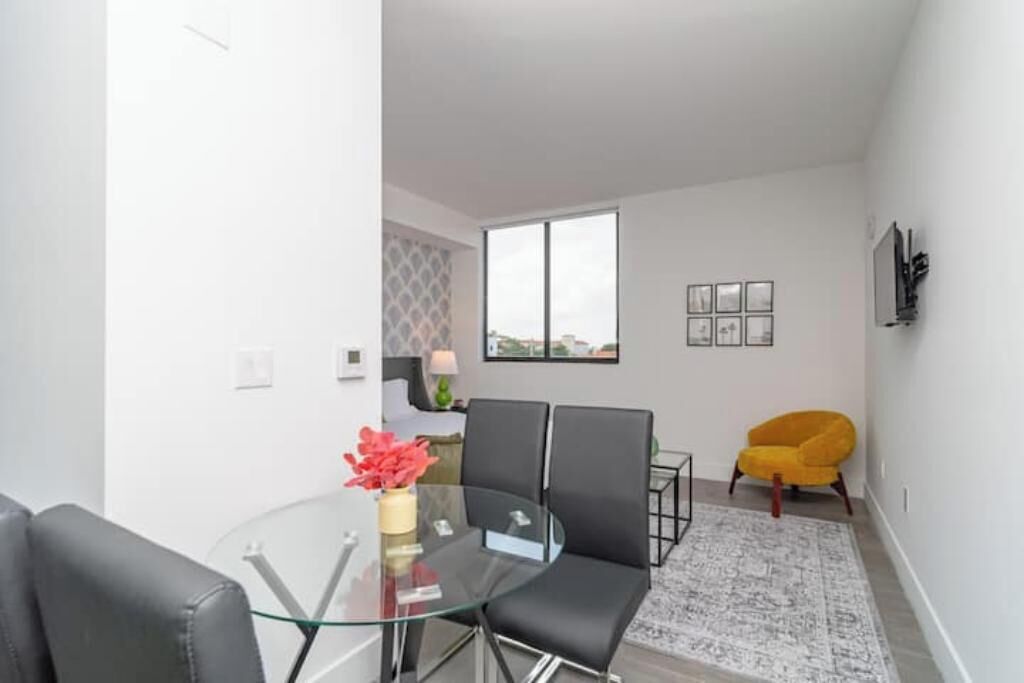Un salon moderne avec une table à manger en verre, des chaises noires, un fauteuil jaune et un tapis à motifs.
