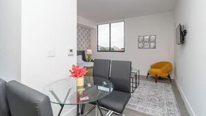 A modern living room with a glass dining table, black chairs, a yellow armchair, and a patterned rug. - King Bed brand new safe Oasis minutes to Brickell (Miami)