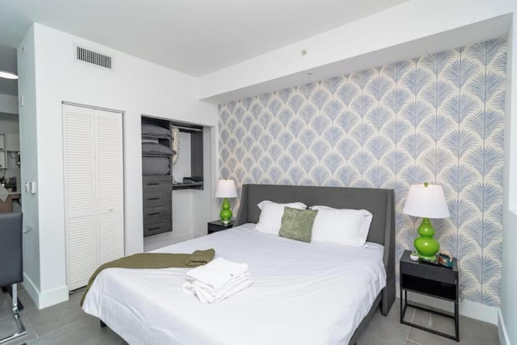 Une chambre bien rangée, avec un lit, deux tables de chevet dotées de lampes, une armoire et un miroir.