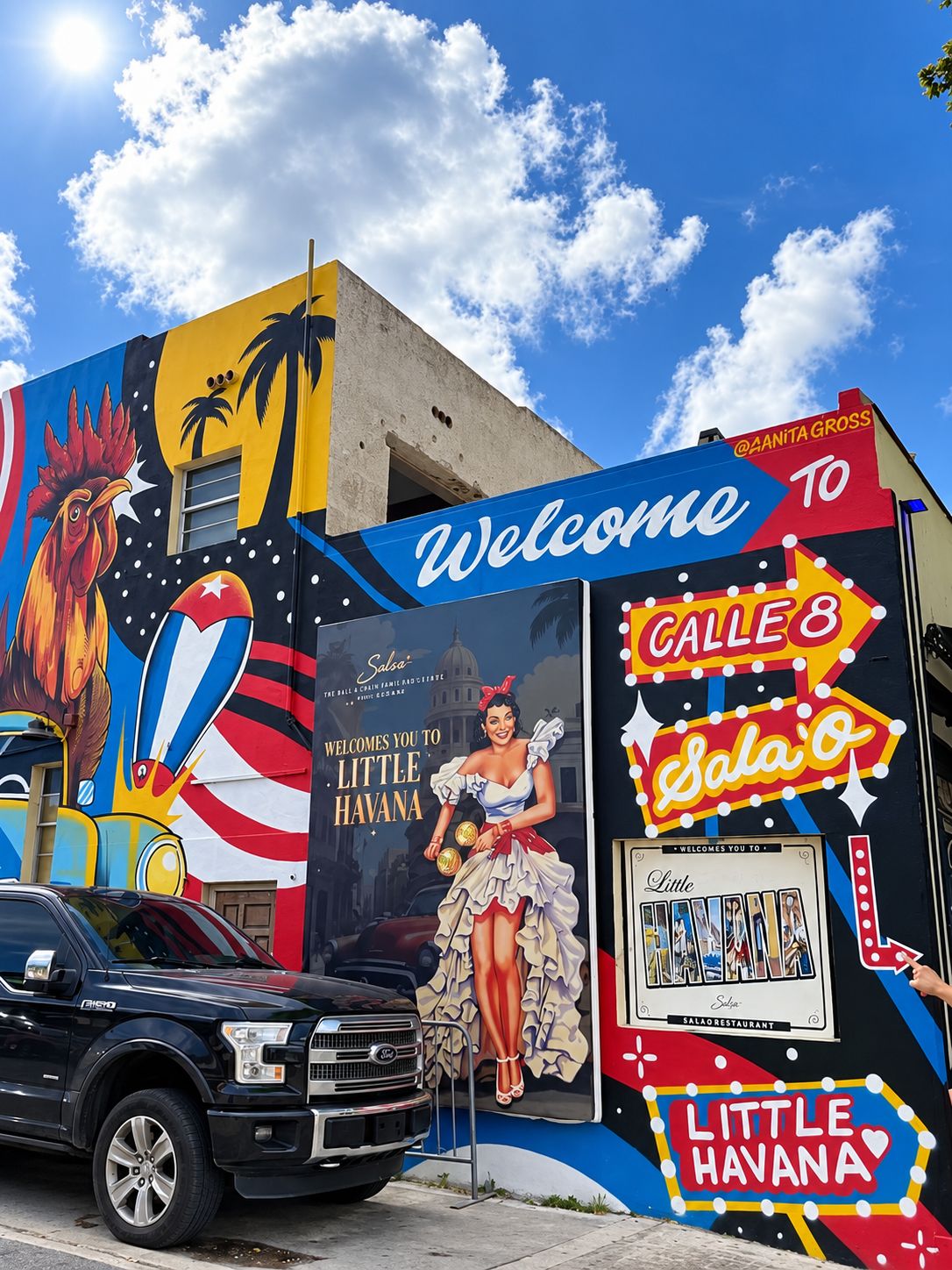 A colorful mural with a rooster, palm trees, and a woman in a dress. It includes text welcoming visitors to Little Havana and mentions Calle 8 and Sala O.