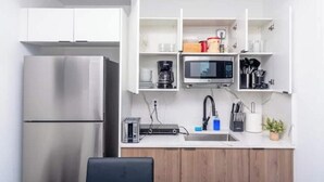 A modern kitchen with white cabinets, a stainless steel refrigerator, a microwave, and a coffee maker.