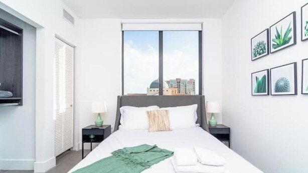 Ein Hotelzimmer mit einem großen Bett, zwei Nachttischen, einem Fenster mit Blick auf die Stadt und gerahmten Pflanzenbildern an der Wand.