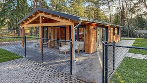 A wooden cabin with a fenced patio area, a covered seating area, and a small table. - Gorgeous home in Meijel with WiFi (Meijel)