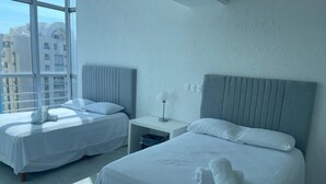 A hotel room with two beds, a nightstand, and a window with a view of buildings. - Apartment with direct access to the beach, fully equipped and renovated. (Acapulco de Juárez)