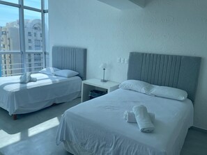 A hotel room with two beds, a nightstand, and a window with a view of buildings. - Apartment with direct access to the beach, fully equipped and renovated. (Acapulco de Juárez)