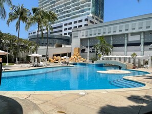 A swimming pool with lounge chairs and palm trees, surrounded by modern buildings. - Apartment with direct beach access, fully equipped and renovated. (Acapulco de Juárez)