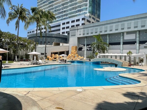 A swimming pool with lounge chairs and palm trees, surrounded by modern buildings.