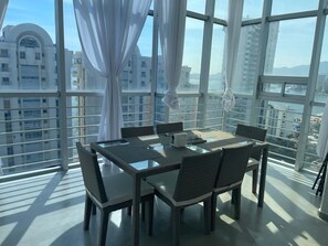 A dining area with a table and chairs, large windows, and a view of buildings. - Apartment with direct access to the beach, fully equipped and renovated. (Acapulco de Juárez)