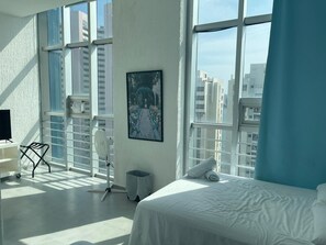 A hotel room with a large window, a bed, a desk, and a chair.