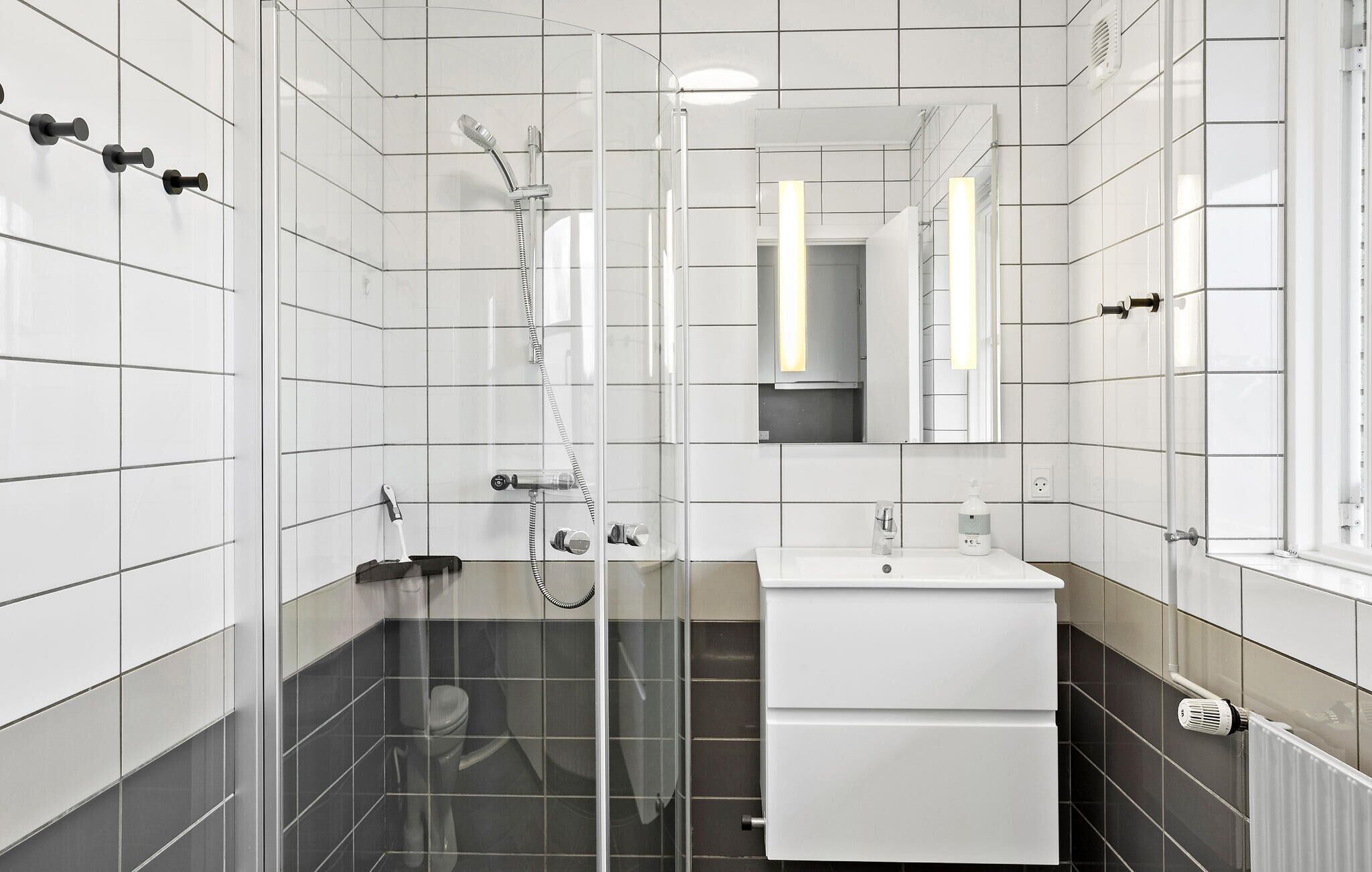 A modern bathroom with white tiles, a glass shower enclosure, a white sink, and a mirror.