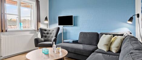 A modern living room with a grey sofa, a round wooden coffee table, and a blue brick wall.