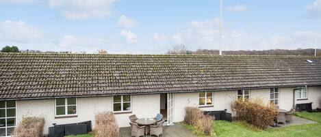 A single-story building with a tiled roof, a patio with outdoor furniture, and a grassy yard.