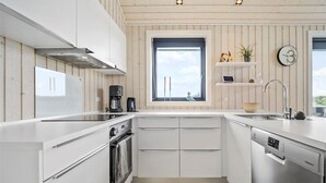 Une cuisine moderne avec des meubles blancs, un four encastré, un lave-vaisselle et une fenêtre offrant une belle vue.