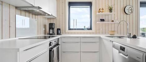 A modern kitchen with white cabinetry, a built-in oven, a dishwasher, and a window with a view.