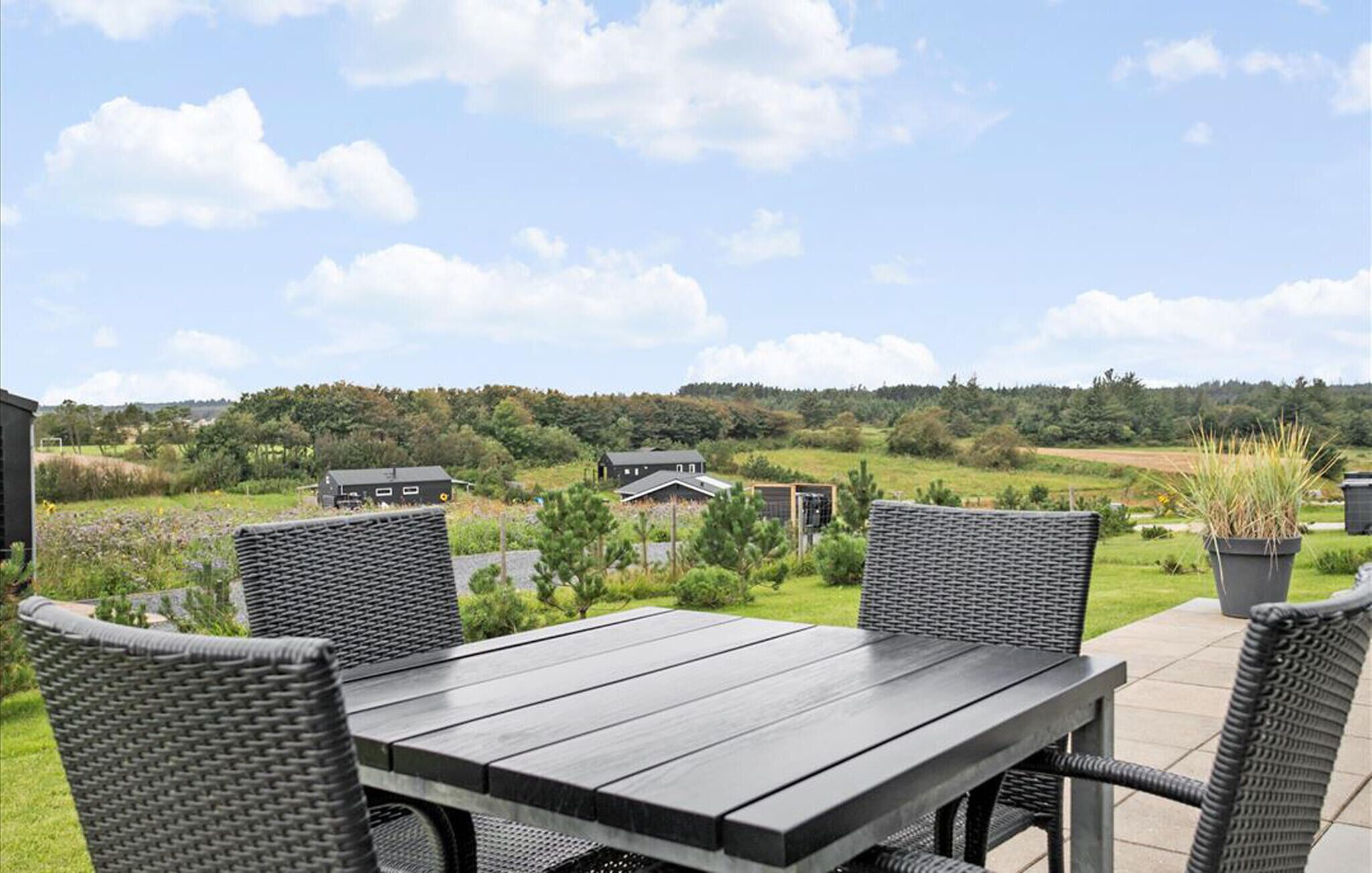 An outdoor patio with a table and chairs, overlooking a rural landscape with houses and fields.