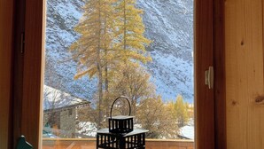 L’intérieur d’un chalet en bois, avec une fenêtre donnant sur une montagne enneigée et un arbre.