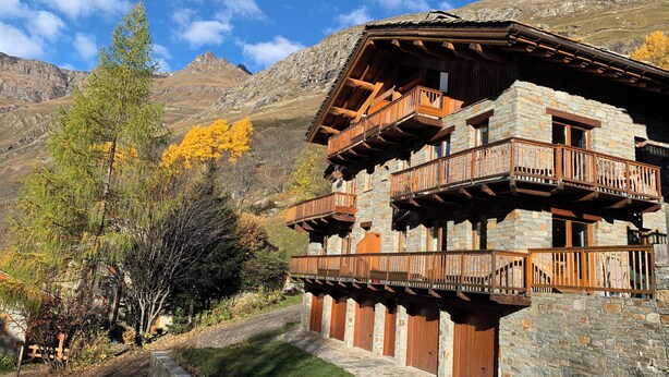 Un bâtiment en pierre doté de balcons en bois, avec une chaîne de montagnes en arrière-plan.