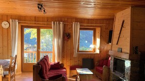 Un chalet confortable avec des murs en bois, une cheminée, un canapé, une table et une horloge au mur.