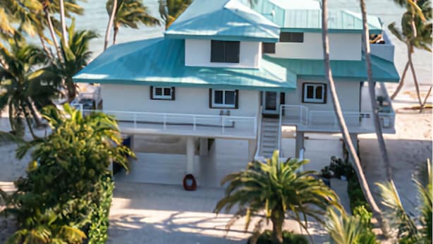 A beachfront property with a two-story building, a covered porch, and palm trees. - Beautiful ocean front private beach 2-bedroom house gorgeous views Isla morada  (Islamorada)