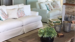 A living room with a white sofa, a wooden coffee table with a plant, and a large mirror reflecting the room. - Beautiful ocean front private beach 2-bedroom house gorgeous views Isla morada  (Islamorada)
