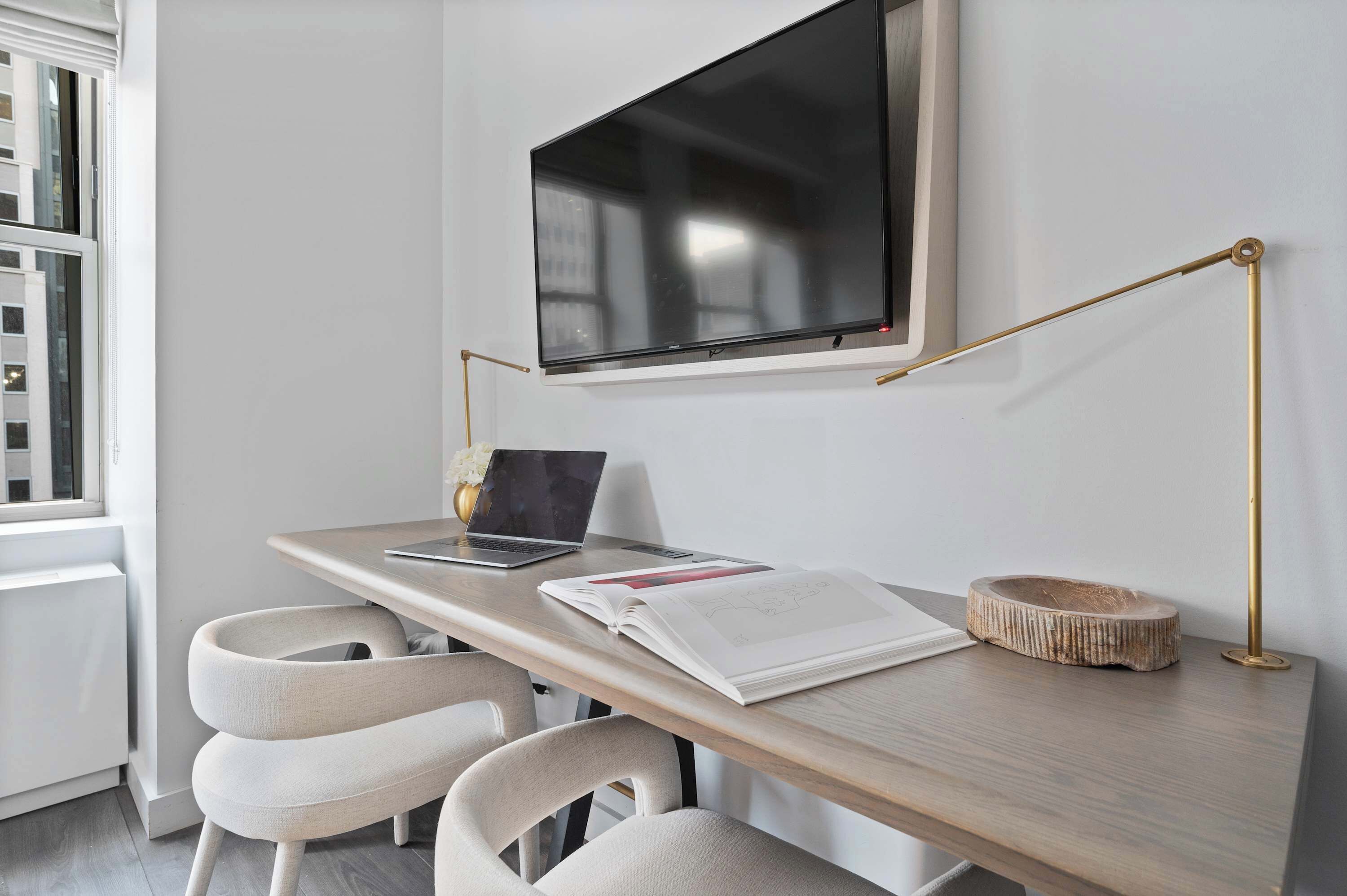 Un espacio de trabajo moderno con escritorio, sillas, una computadora portátil, un libro y una televisión.