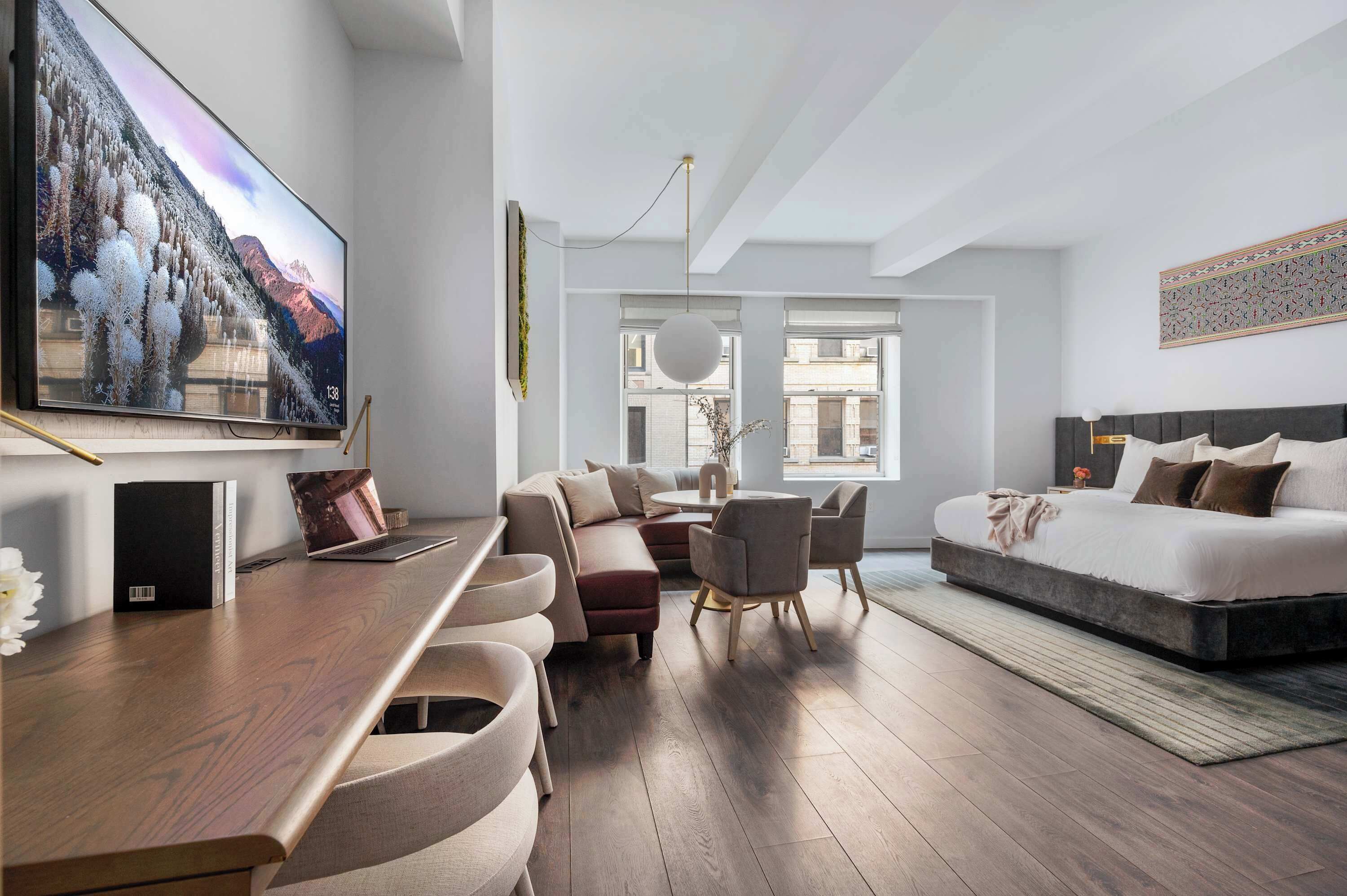 A modern hotel room with a large flat-screen TV, a sofa, a dining area, and a bed.