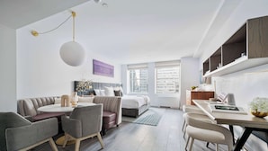 Una habitación de hotel moderna con sofá, mesa de comedor, sillas, cama y estanterías empotradas.