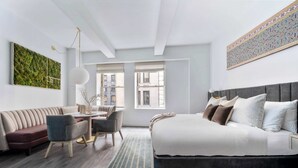 Quarto de hotel moderno com cama, sofá, mesa de jantar, cadeiras e obras de arte nas paredes.