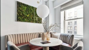 Um interior moderno com uma mesa redonda, assentos acolchoados, uma obra de arte com parede verde e uma janela com vista para a cidade.