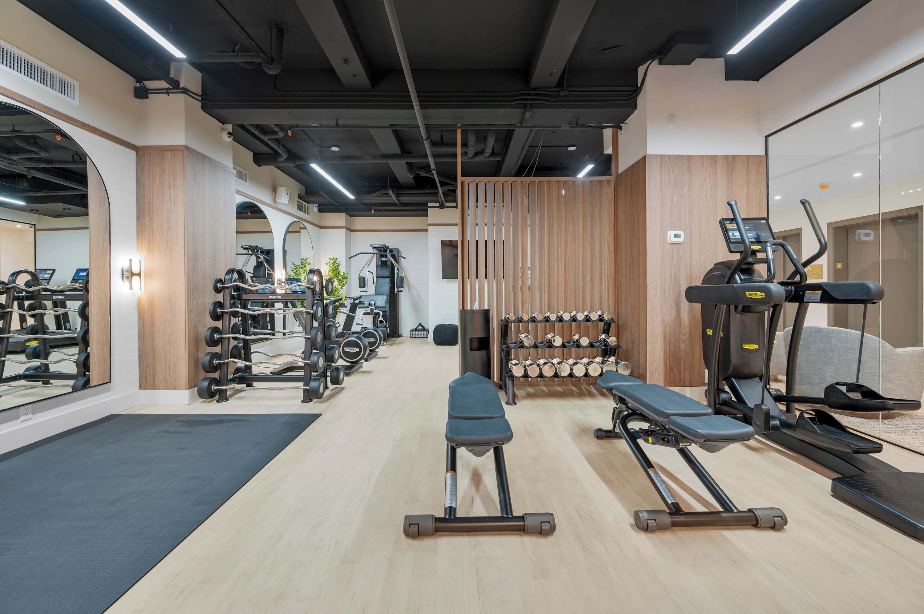 Un gimnasio con equipamiento de ejercicio, una banca, cintas de correr y un espejo grande.