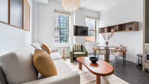 A modern living room with a sofa, a dining table with chairs, a TV, and a decorative vase. - 17John: Luxury One Bedroom Apartment (New York)