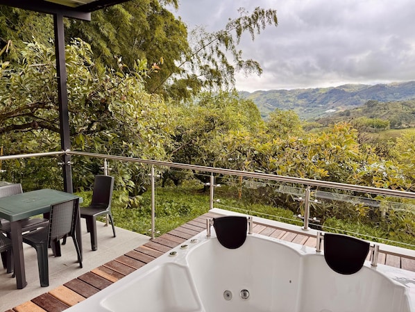 A balcony with a hot tub, outdoor seating, and a view of a mountainous landscape.