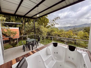 A covered outdoor area with a hot tub, seating, and a view of a mountainous landscape.