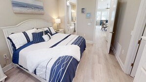 A bedroom with a large bed, a bedside table with a lamp, a bathroom visible through an open door, and a dining area in the background. - Treasure Cay Getaway with BOAT DOCK!
4 bedroom, pool, & bbq Cabana (Treasure Cay)