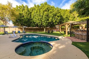Relax by the oval-shaped pool with a hot tub, surrounded by lounge chairs and lush greenery.