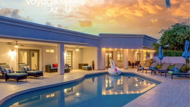 A poolside area with lounge chairs, a pool, and a building with illuminated windows. - Scottsdale Vacation Home Near Kierland|Heated Pool & Games (Scottsdale)