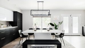 A modern dining area with a white table, black chairs, and a black bench. There is a chandelier above the table and a plant on the windowsill. - Scottsdale Vacation Home Near Kierland|Heated Pool & Games (Scottsdale)