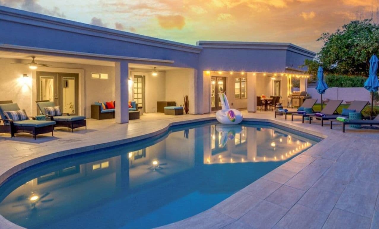 A poolside area with lounge chairs, a pool, and a building with illuminated windows.