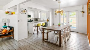 Een ruime woonkamer met een houten eettafel, gele stoelen en een moderne keuken op de achtergrond.