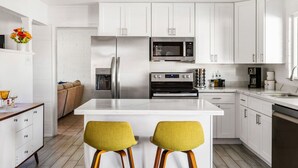 Een moderne keuken met witte kasten, roestvrijstalen apparatuur en een centraal eiland met twee gele stoelen.