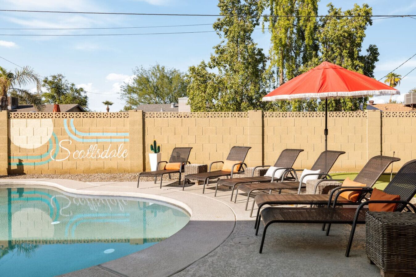 A pool area with lounge chairs and a red umbrella.