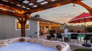 Een hottub, zitplaatsen buiten en een zwembadgedeelte onder een houten pergola.