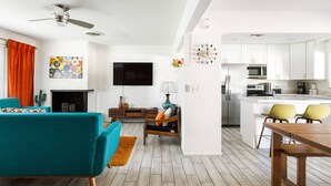 Een moderne woonkamer met een open haard, een blauwgroene bank, een houten salontafel, en een keuken met witte kasten en roestvrijstalen apparatuur.