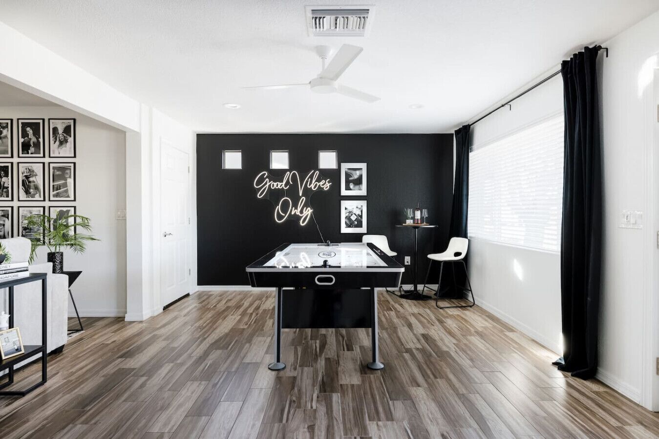 Un salon moderne avec un baby-foot, un mur noir orné de photos encadrées et un ventilateur de plafond.
