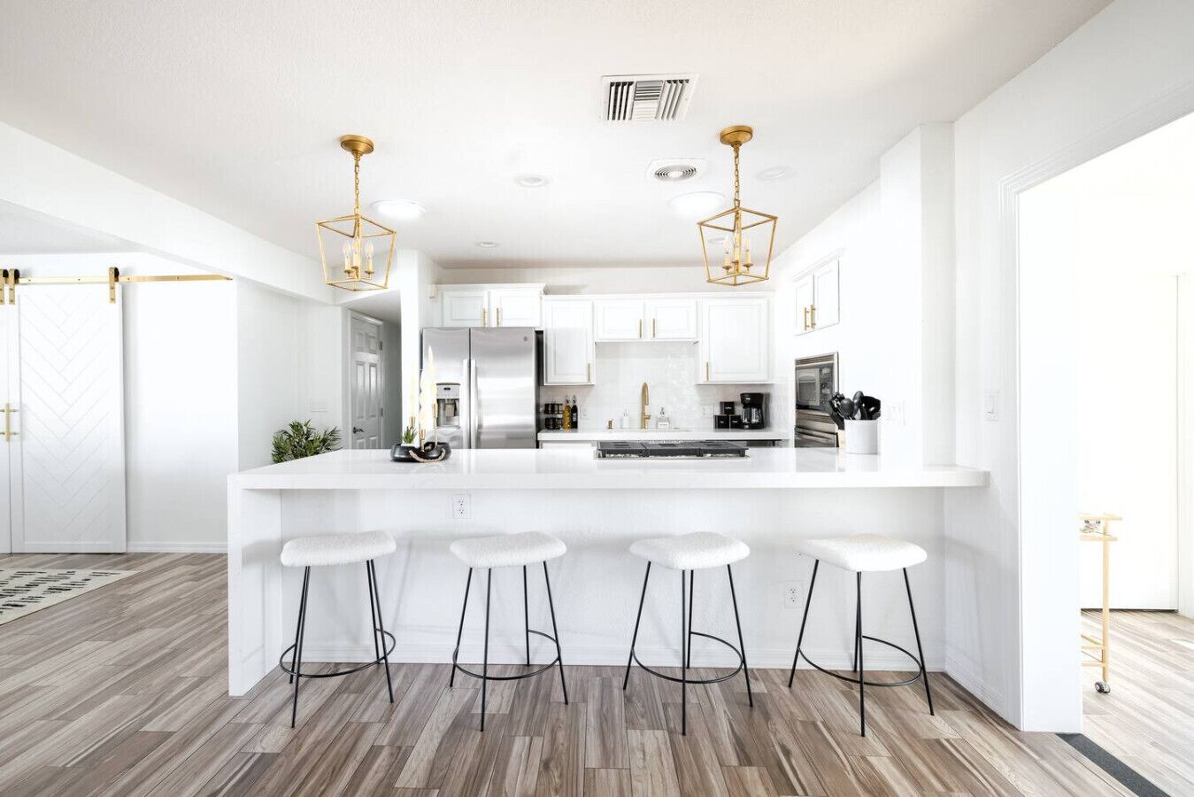 A modern kitchen with white cabinetry, a central island with stools, and pendant lighting.